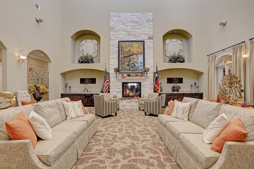 Interior image of Woodhaven Village's common area. There are comfortable couches, chairs, and a roaring fireplace.