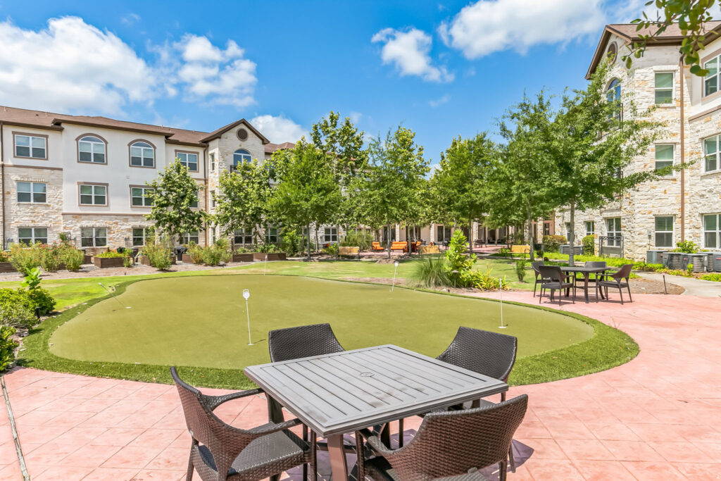 The courtyard features a large putting green and multiple patio seating areas at Woodhaven Village, a senior living community near Montgomery, TX.