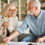 April 25 Events Page Image - Woodhaven Village Elderly man and woman smiling and holding small dog